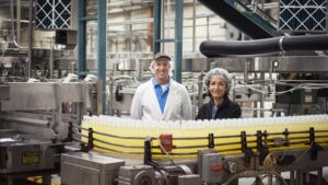 Two workers by a conveyor belt of lemon flavored water in a bottling plant.